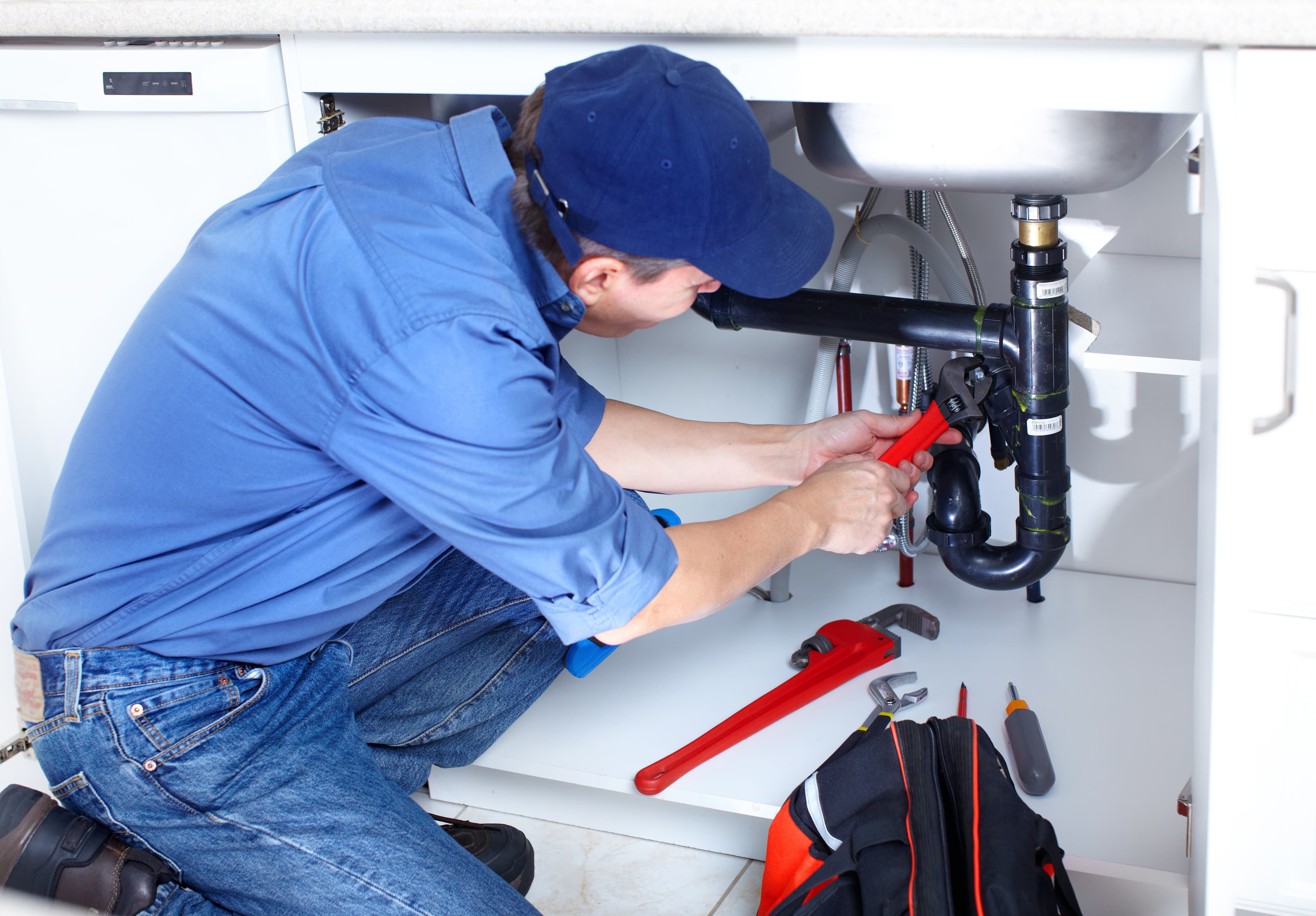 Plumber fixing pipes under a kitchen sink